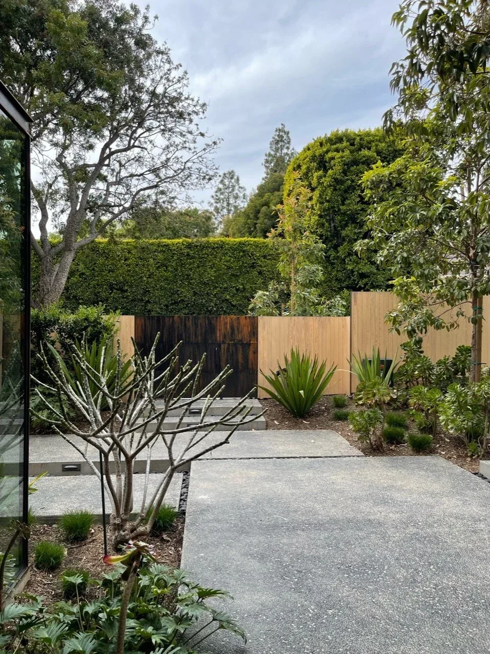 Concrete patio area with stepping slabs and landscaped greenery enclosed by wooden fence and hedge