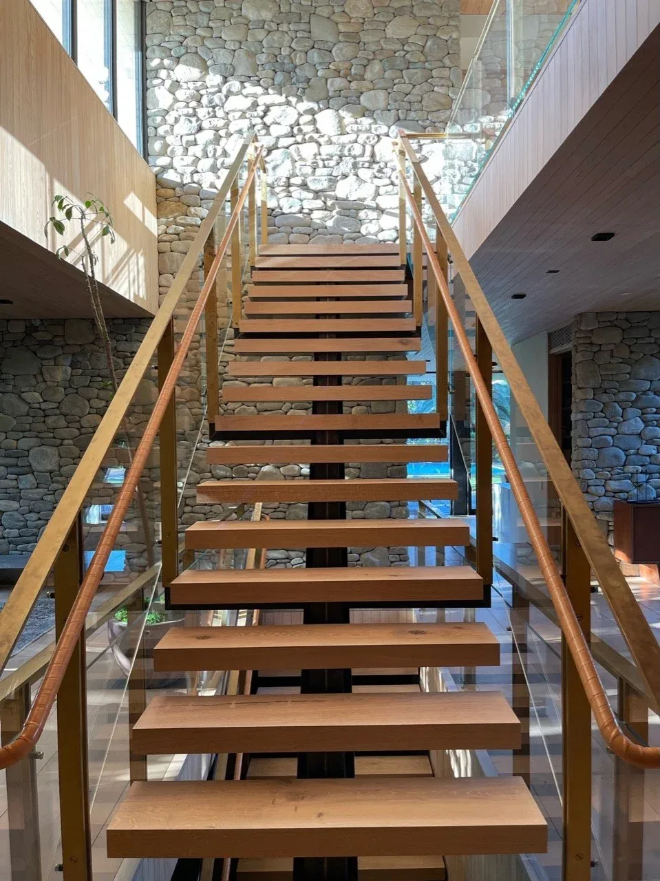 Floating wood staircase with glass panels and wood handrails, adjacent to stone walls.