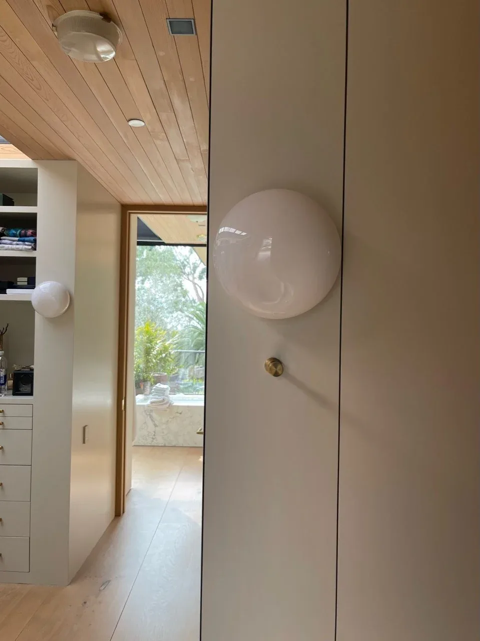 Hallway interior showing integrated cabinetry and wall sconces with a view through a doorway to an outdoor area.