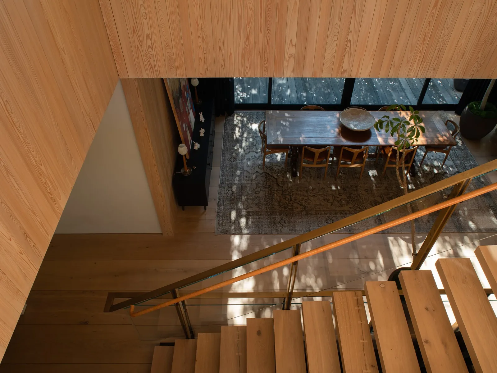 View from stair landing showing wooden dining area with glass railing and wood-paneled walls.