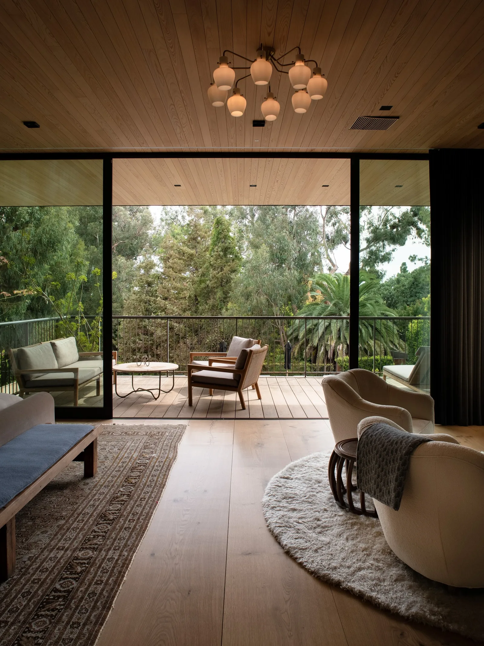 Living room with floor-to-ceiling sliding glass doors opening to a balcony with outdoor seating and trees beyond.