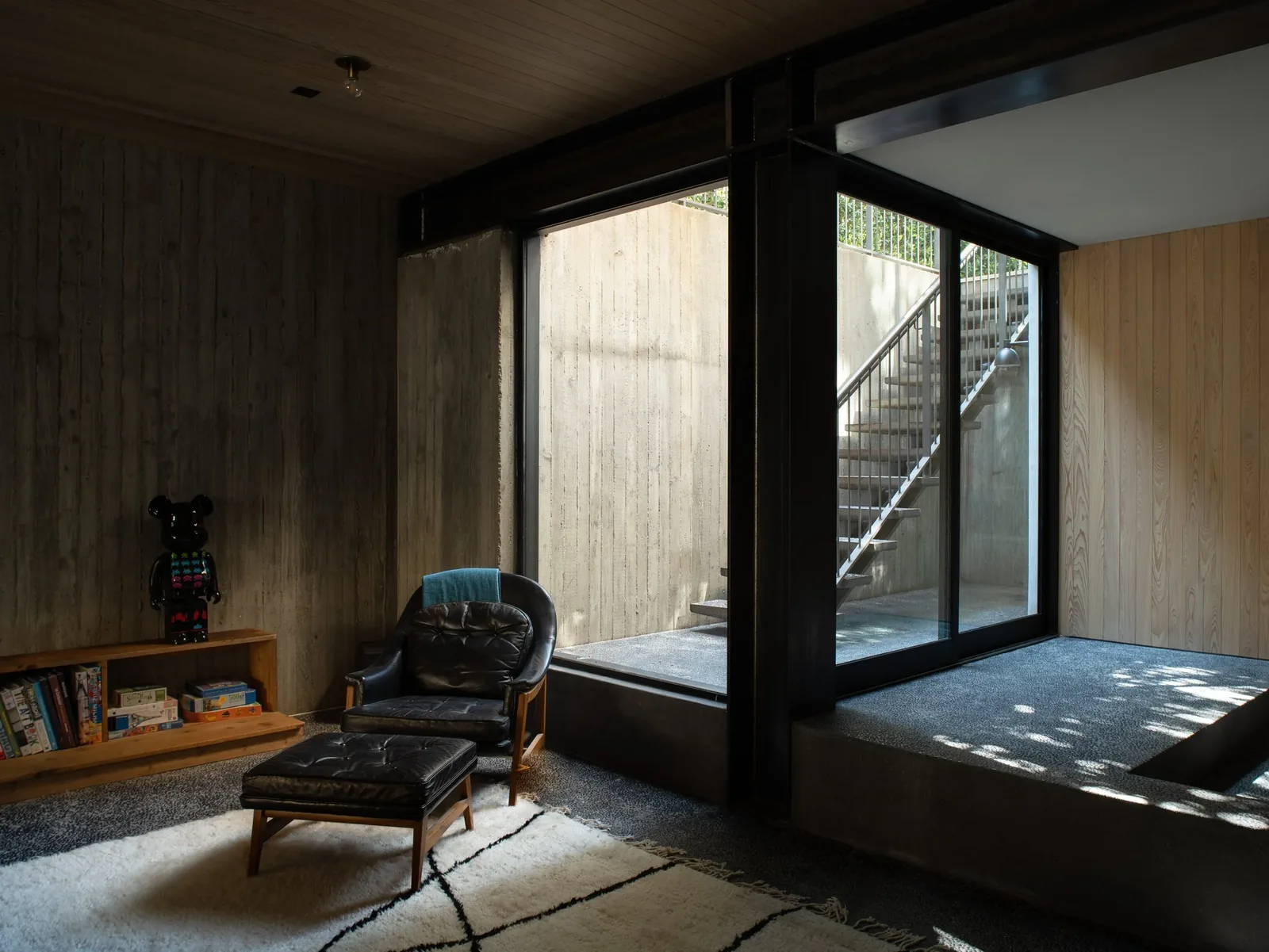 Living area features textured concrete wall, leather seating, wooden bookshelf and large sliding glass door opening to exterior stairs.