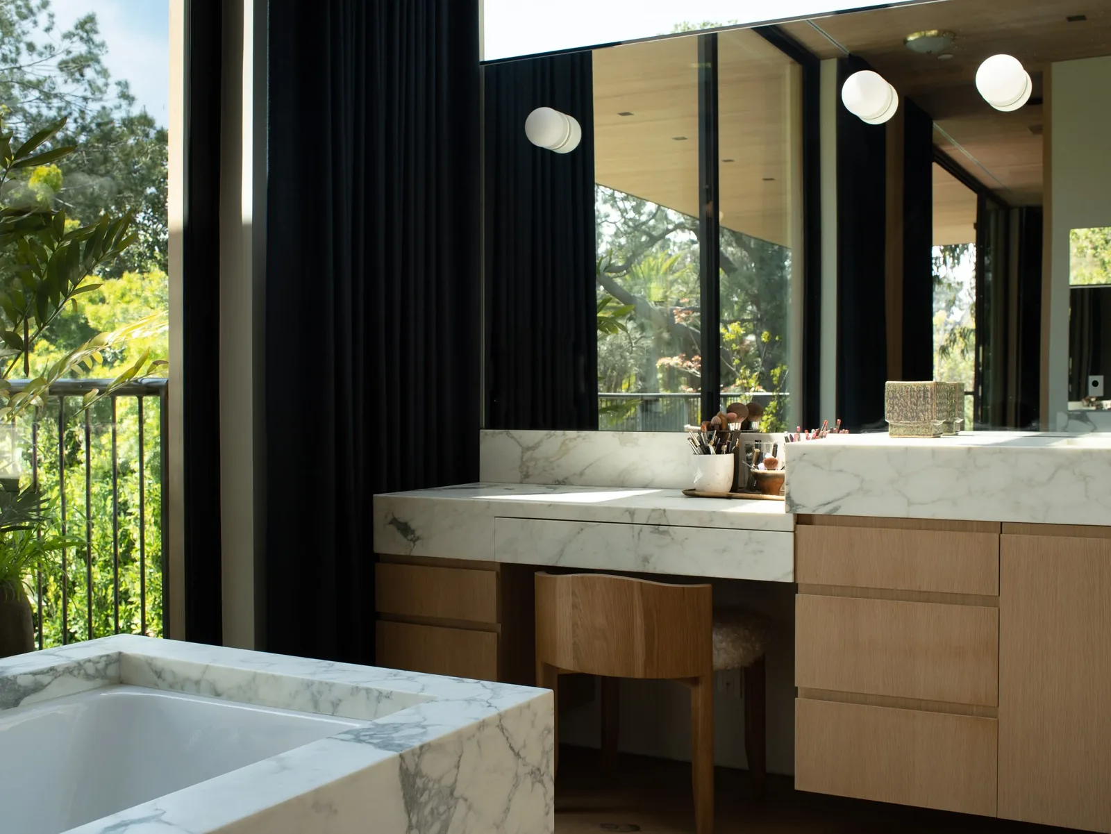 Bathroom featuring a marble countertop vanity with wooden cabinets and a matching marble bathtub beside a large window with dark curtains.