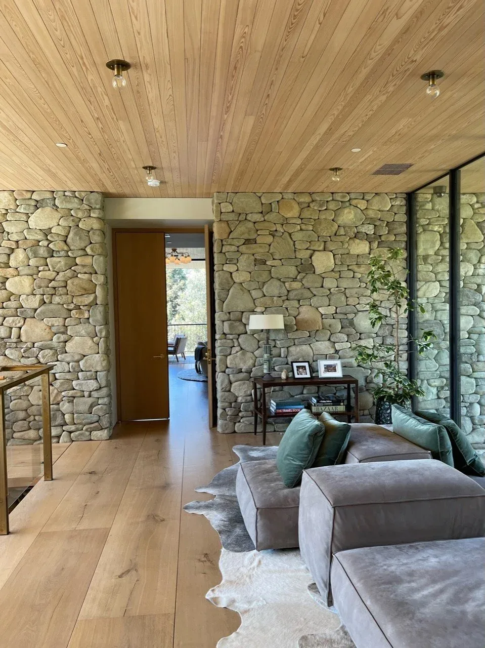 Living room features river stone accent walls, hardwood flooring and ceiling, and a sectional sofa with green pillows.