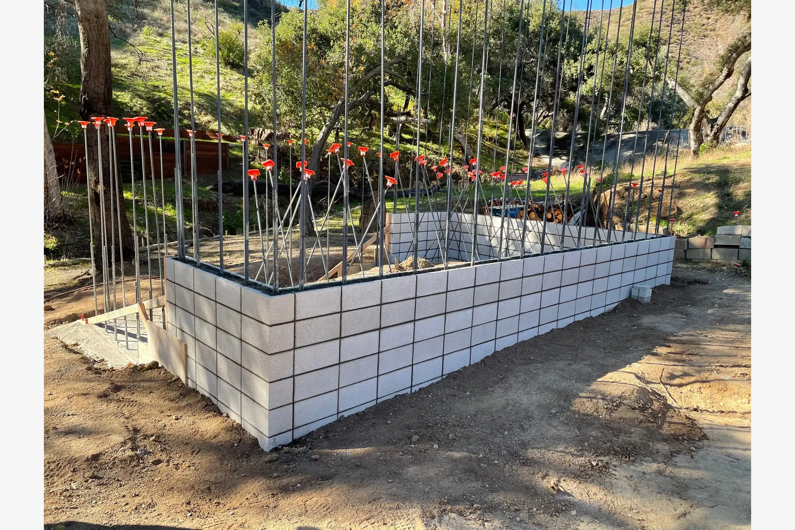 Foundation work featuring concrete block walls and vertical rebar reinforcement at a hillside site.