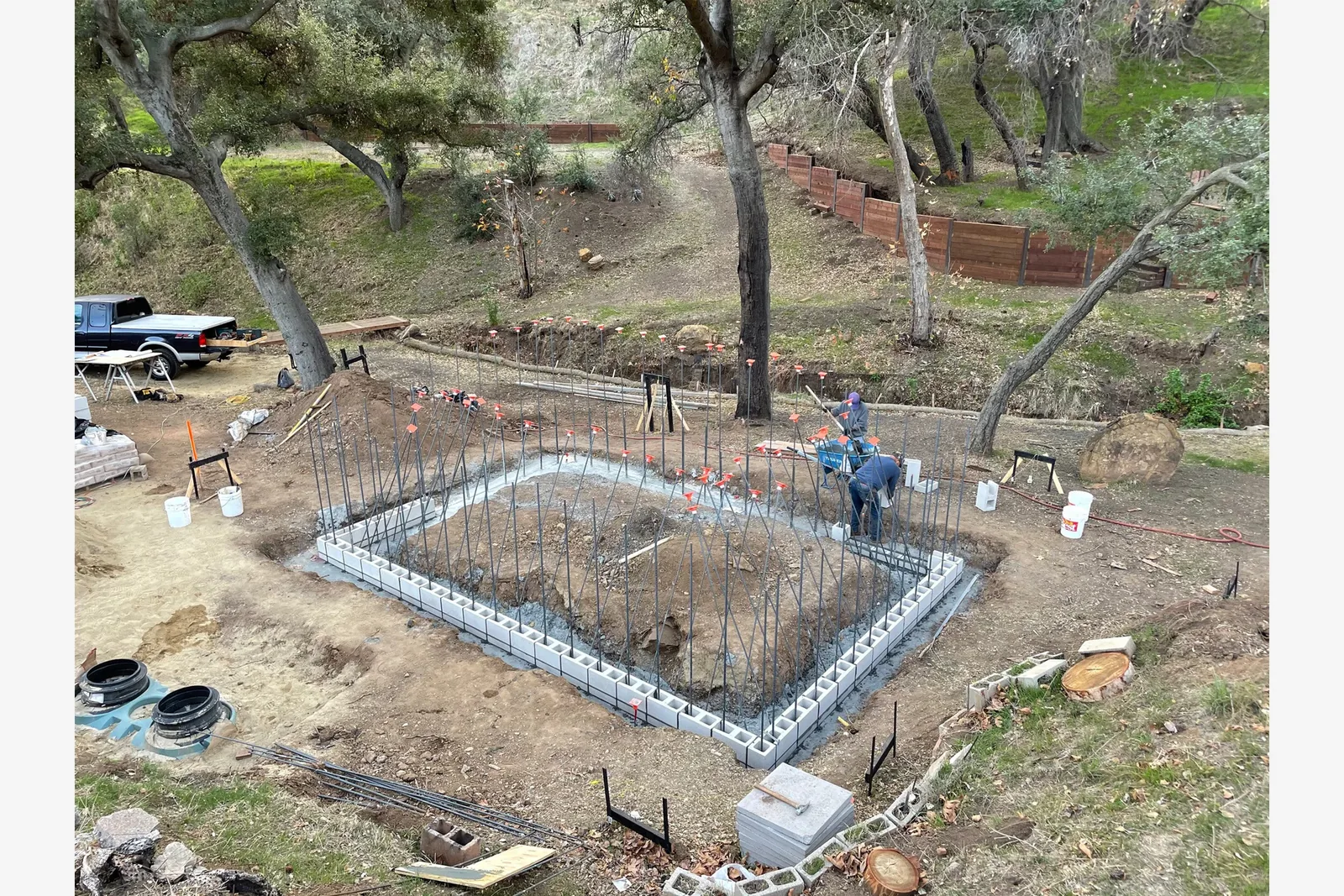 Foundation work with concrete block walls and vertical rebar at a construction site in a wooded area.
