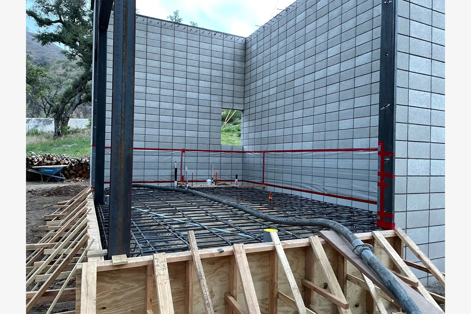 Concrete block walls and steel beam frame with rebar laid out for slab pouring at construction site on wooded terrain.