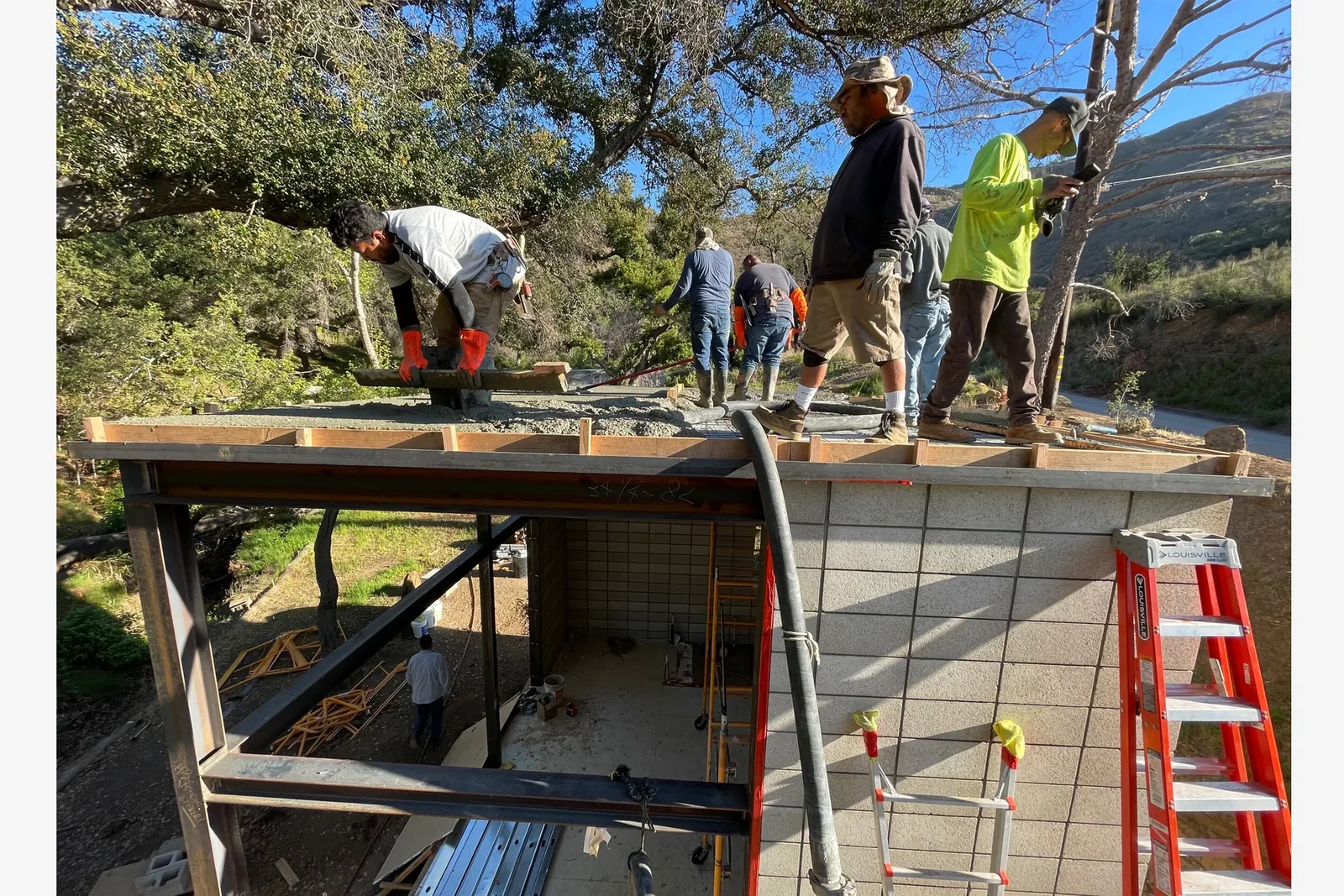Concrete is being poured and smoothed on a roof slab over a steel-framed concrete block structure under construction.
