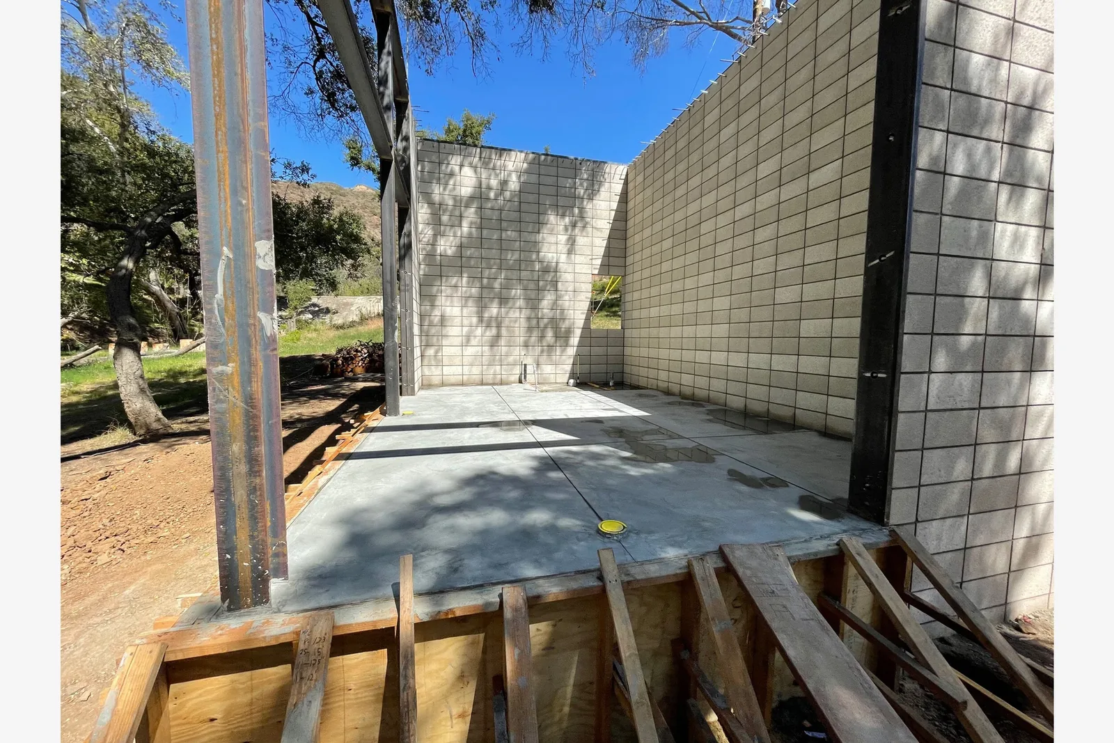 Early construction phase with concrete foundation and block walls framed by steel beams.