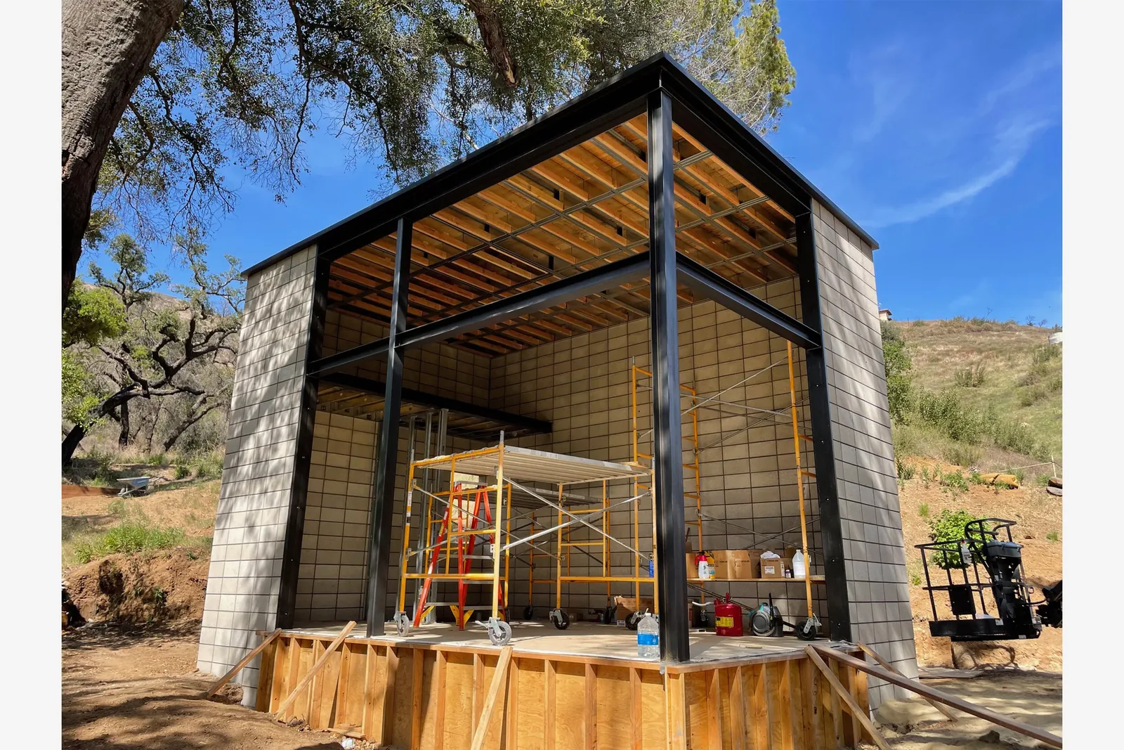 Construction site showing a structure with steel framing and concrete block walls during framing stage.