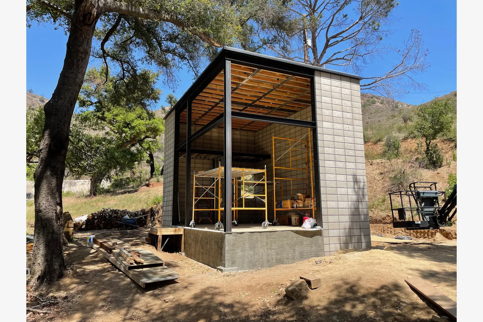 Construction stage of a small building with concrete block walls and exposed steel framing in a natural wooded setting.