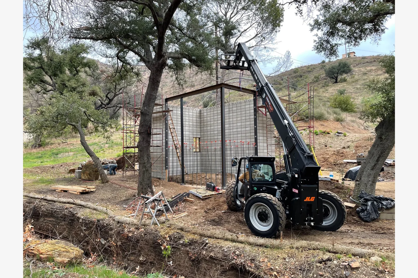 Steel frame and block wall construction on a hillside site with heavy machinery and scaffolding visible.