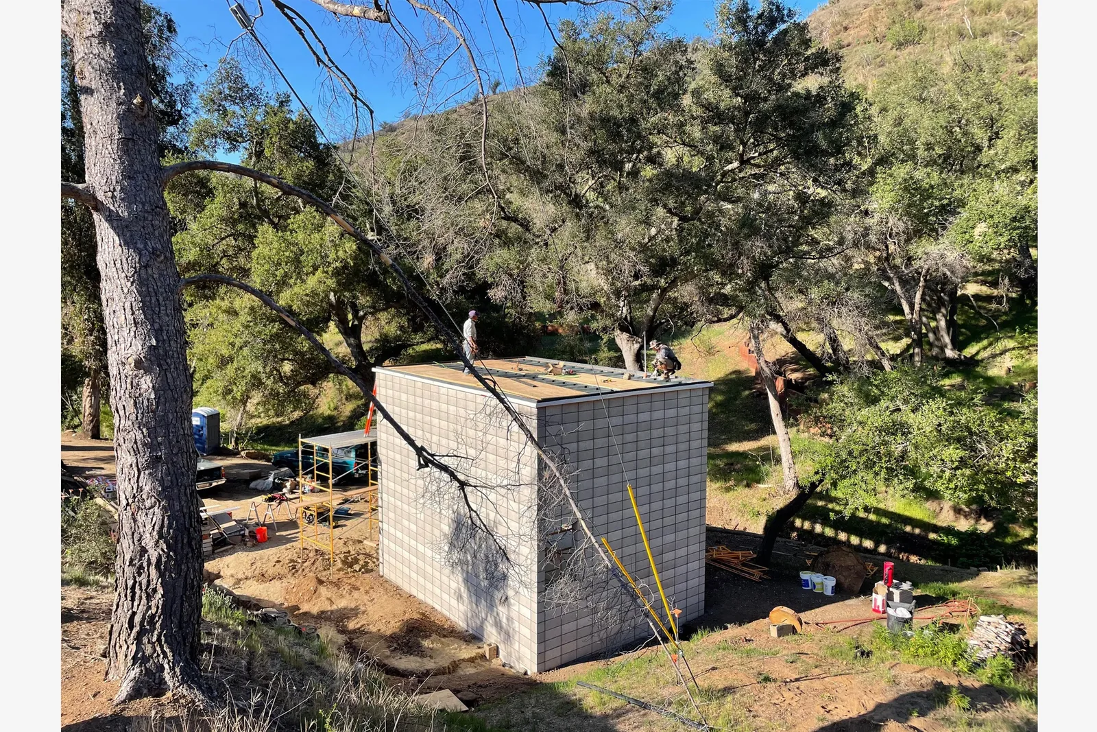 A construction site with a simple cinder block structure and scaffolding in a rural landscape.
