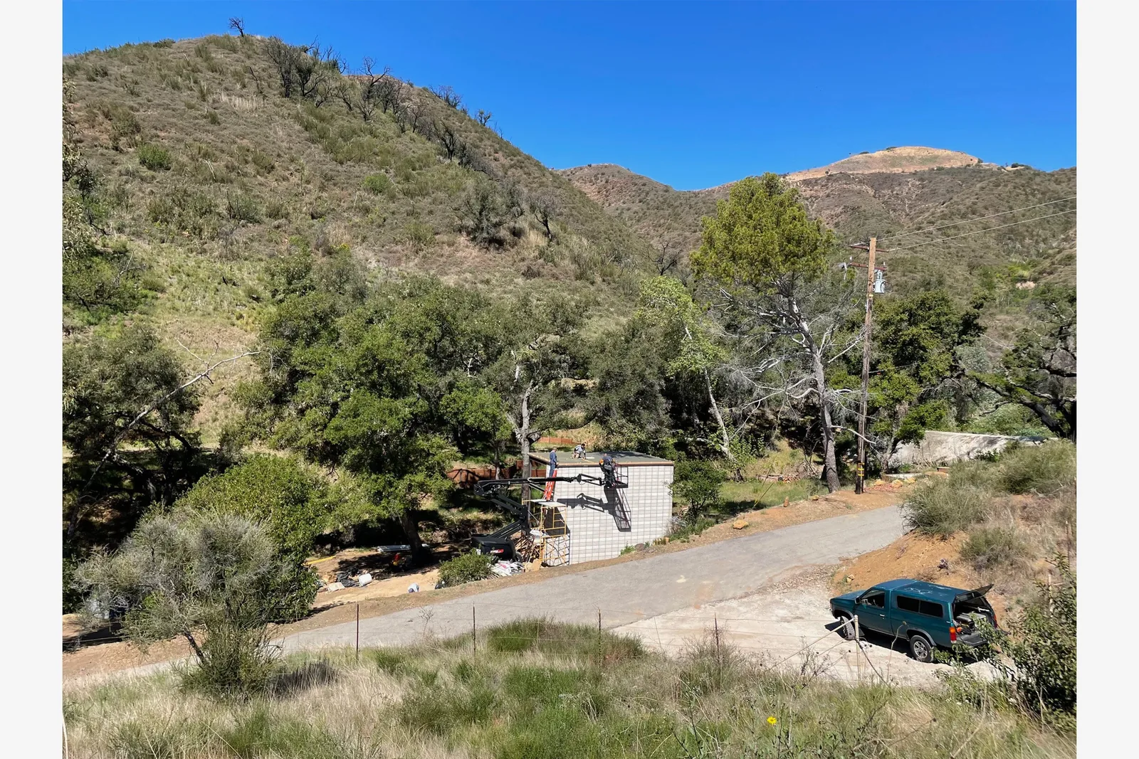 Small block wall structure under construction at a hillside site with vegetation and a parked vehicle.