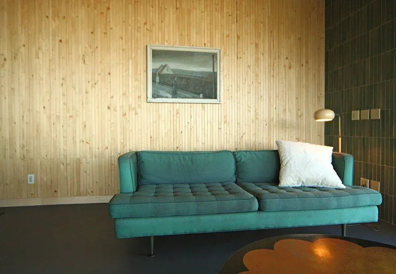 Living room with teal sofa, wood paneled wall, dark tiled wall, and floor lamp.