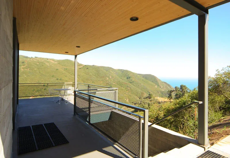 Covered patio with metal railing and wood-paneled ceiling in a hillside house.