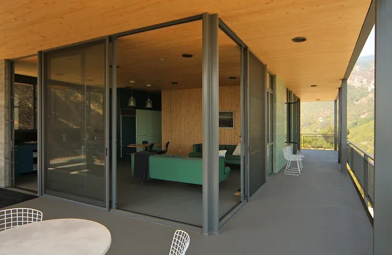 A covered patio with sliding glass doors opens to a living room with wood-paneled ceiling and walls.