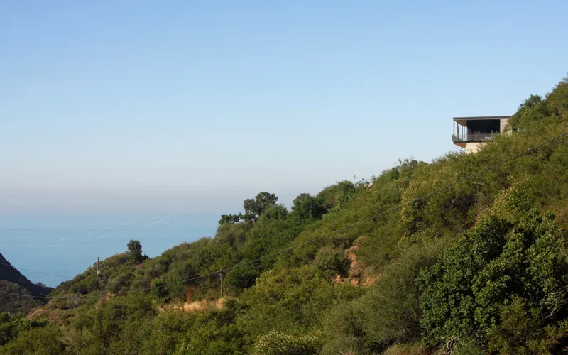 Modern house located on a hillside overlooking a natural landscape with ocean in the distance.