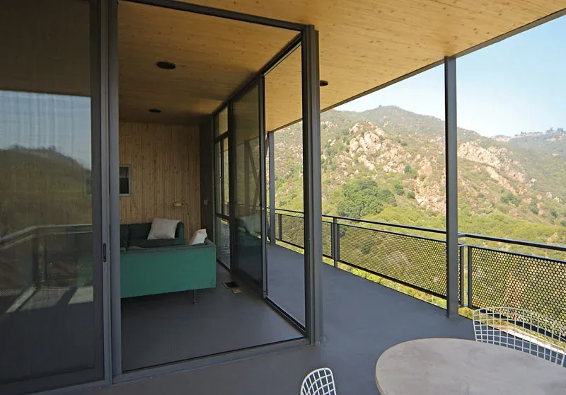 Covered patio adjacent to a living room with floor-to-ceiling sliding glass doors and wood-paneled ceiling.
