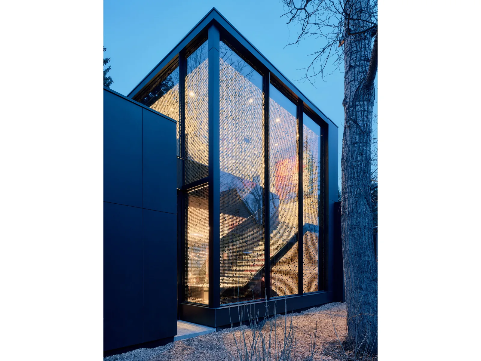 View of the building's exterior corner featuring floor-to-ceiling glass windows showcasing an illuminated staircase inside.