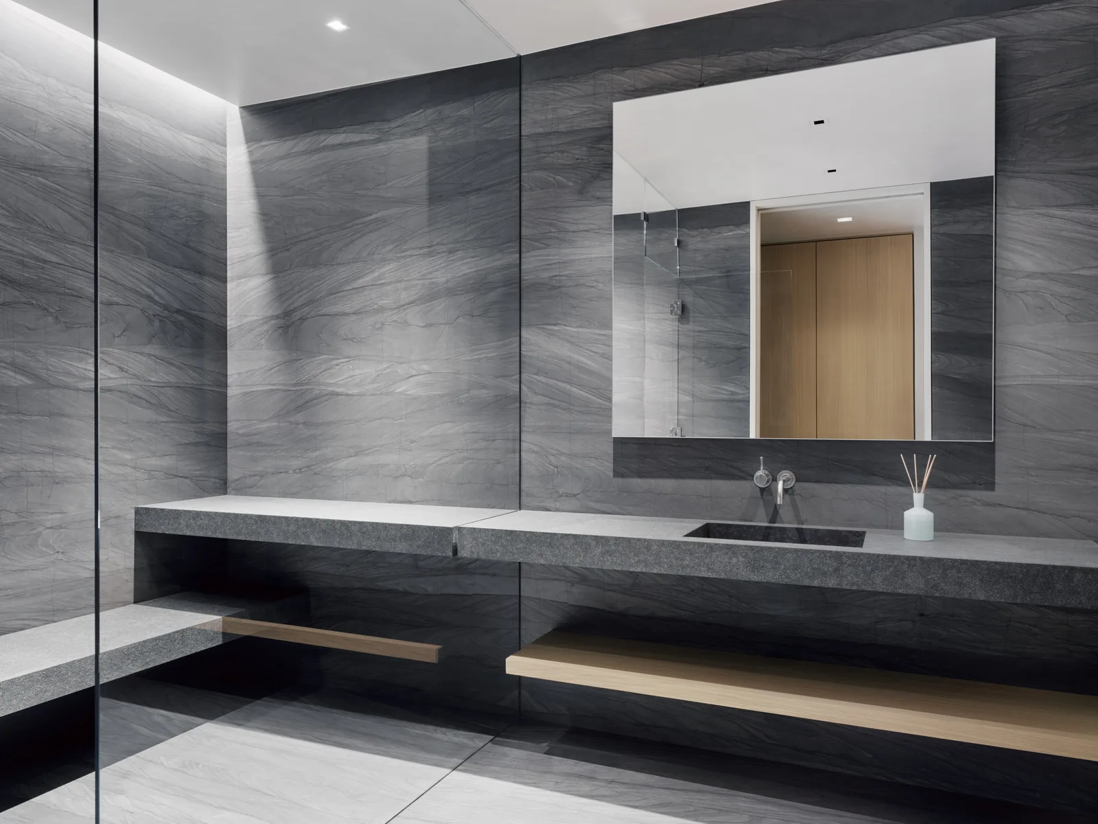 Minimalist bathroom featuring dark gray stone walls, a floating concrete vanity, and a large frameless mirror above the sink.