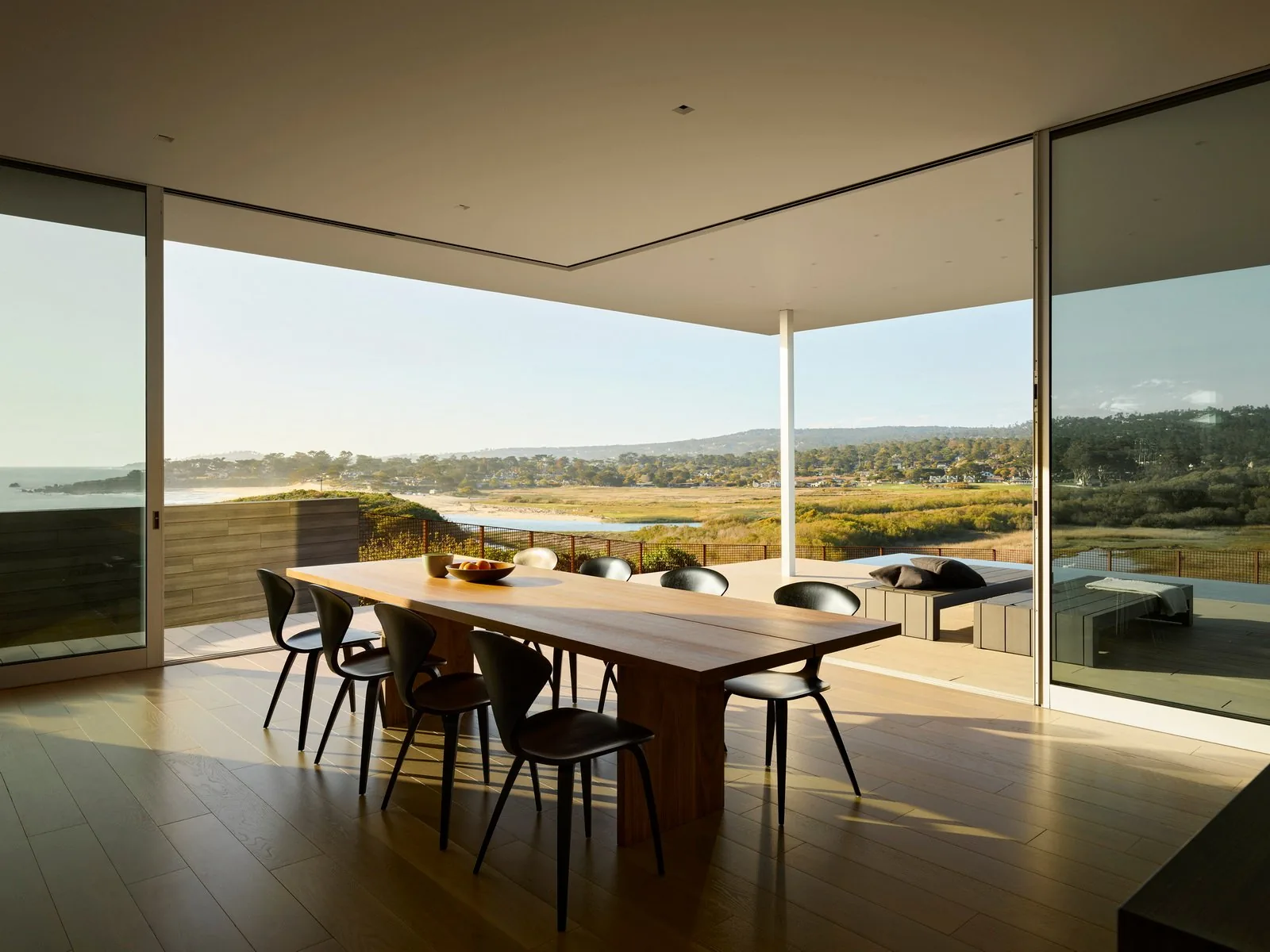 Dining room opening to a covered patio with seating and views of surrounding natural landscape and water body.