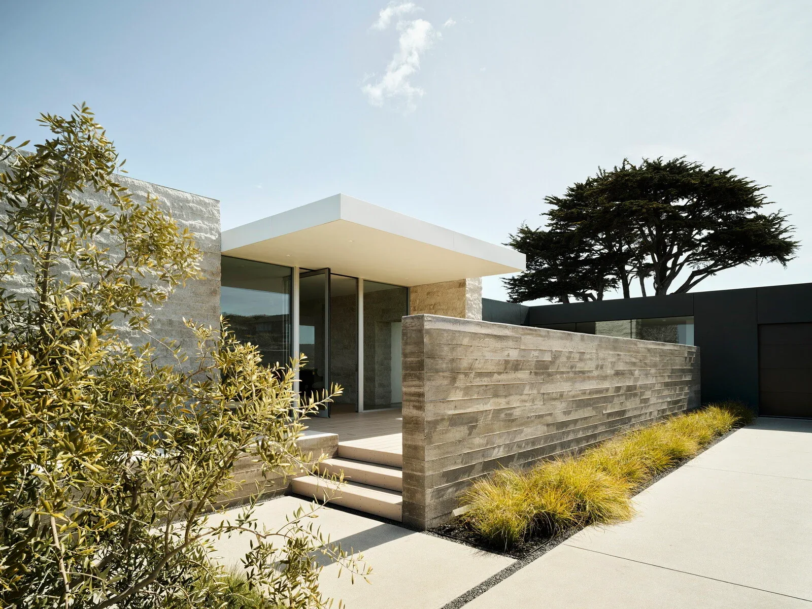Modern house exterior with wood-textured concrete wall and stone cladding under a flat roof.