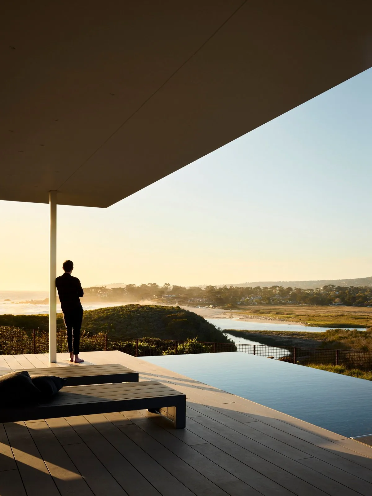 Covered patio with infinity pool overlooking natural landscape at sunset.