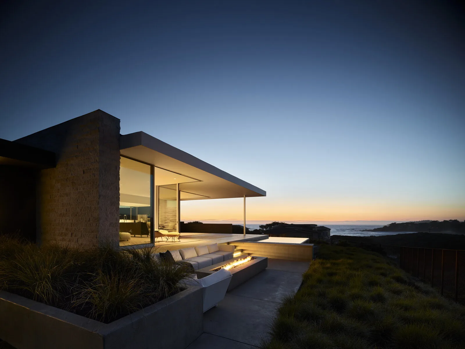Modern house exterior with a cantilevered roof and built-in outdoor fire pit seating at dusk.