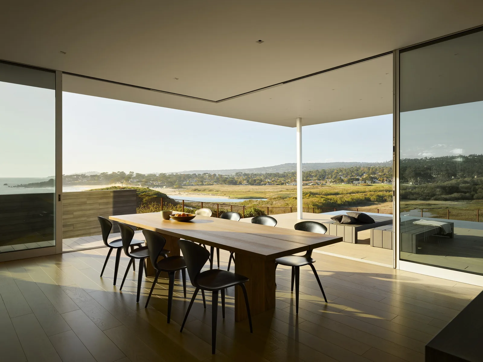Dining room with floor-to-ceiling glazing that opens to a covered patio with views of the surrounding landscape.