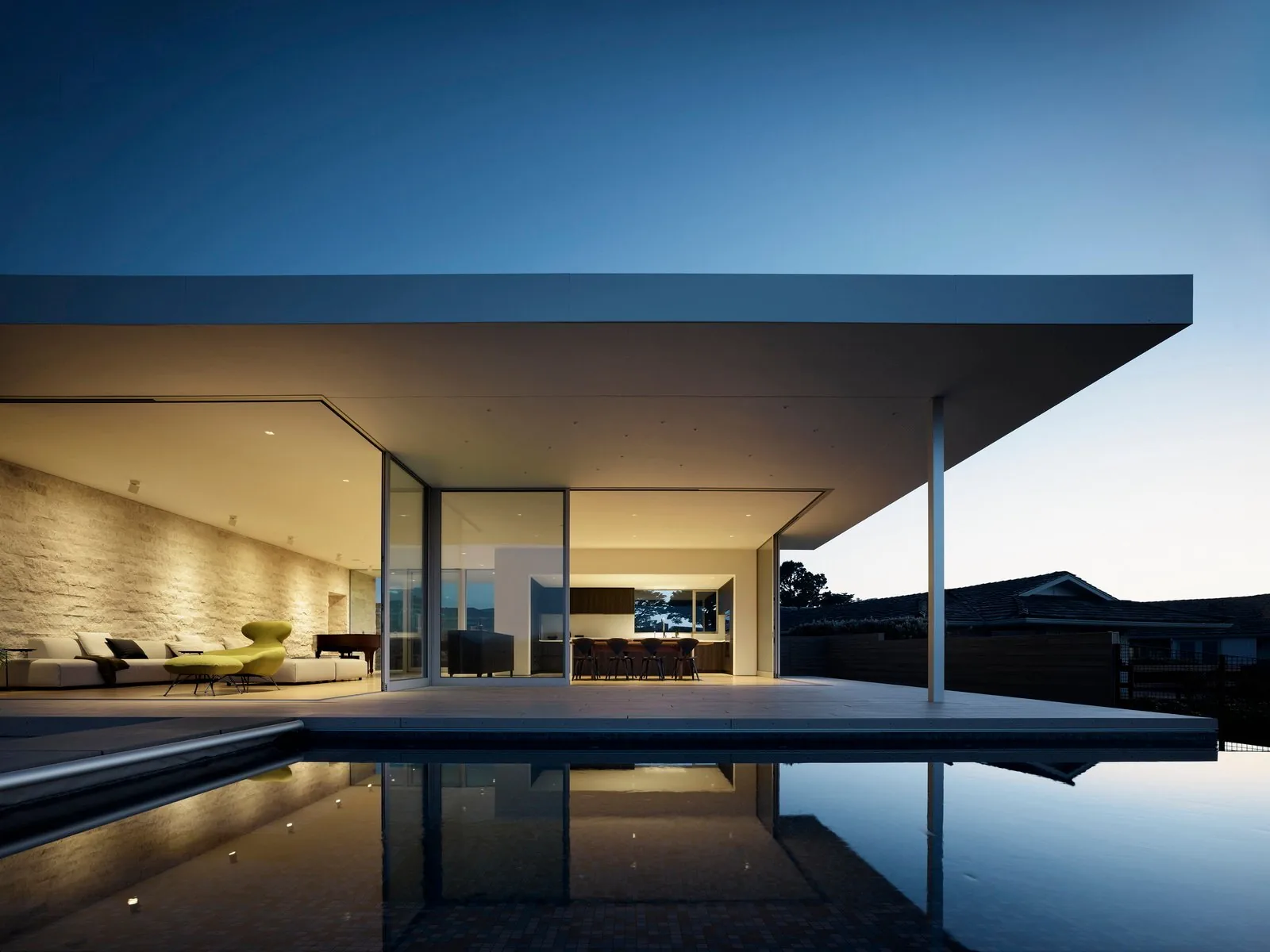 The Ribera Road project features a minimalist open-plan design with floor-to-ceiling glazing and a flat roof extending over a patio and pool.