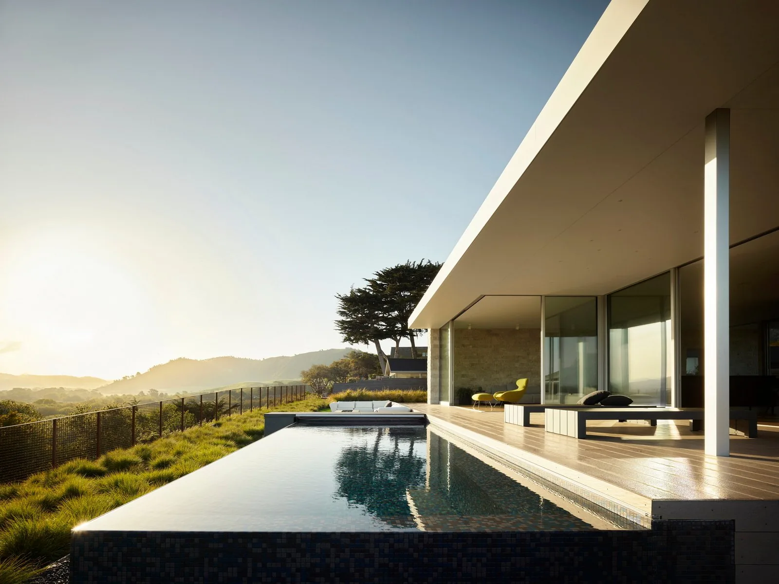 Exterior view of a modern house featuring an infinity pool alongside a covered patio with seating.