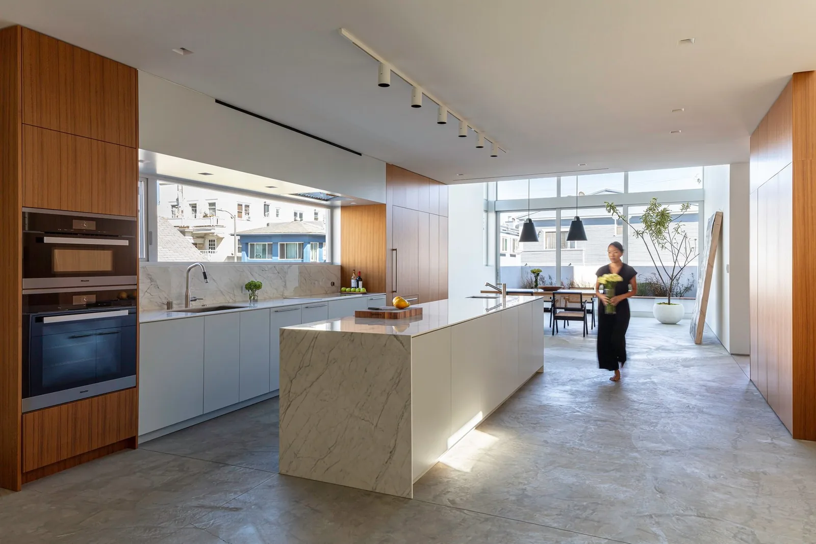 Interior of a kitchen space featuring a marble island, wood-paneled cabinetry, and built-in ovens.