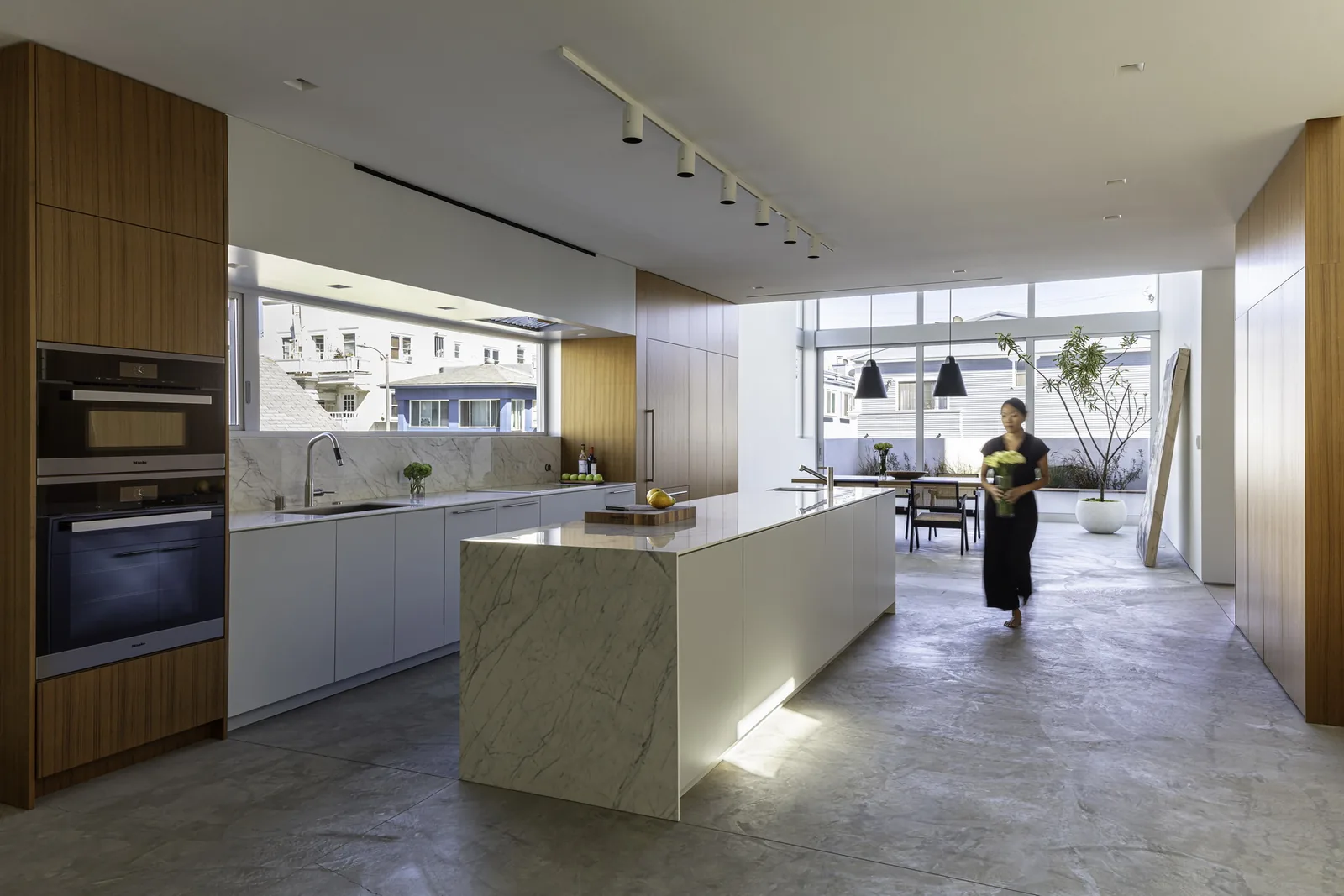 Spacious kitchen features a marble island, wood paneling, and large windows providing natural light.