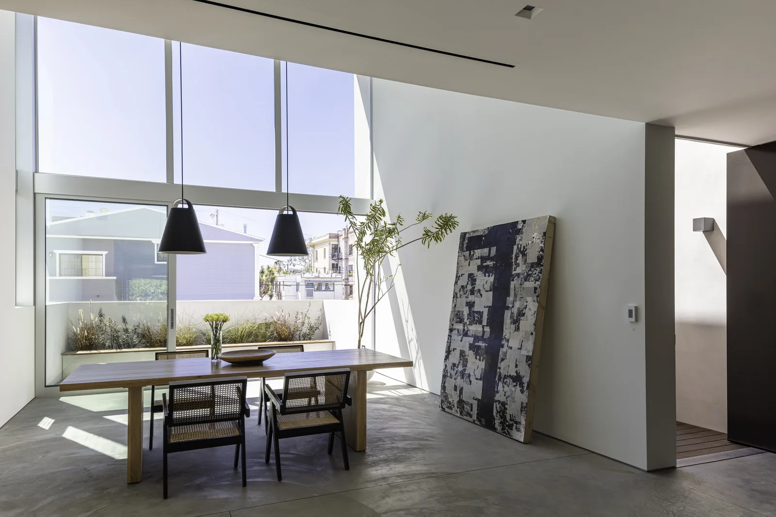 Dining room features floor-to-ceiling glazing, wood furniture, and minimalist decor.