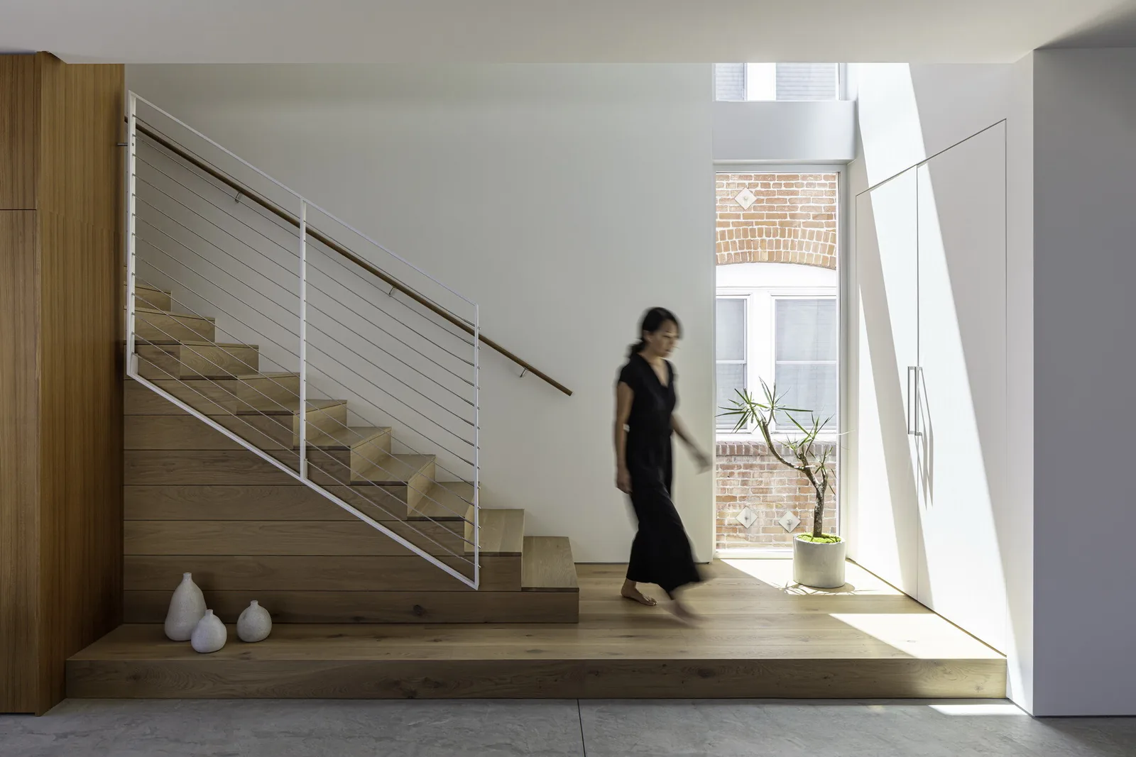 Interior view of a staircase with wooden finish and a tall window with a potted plant in front.