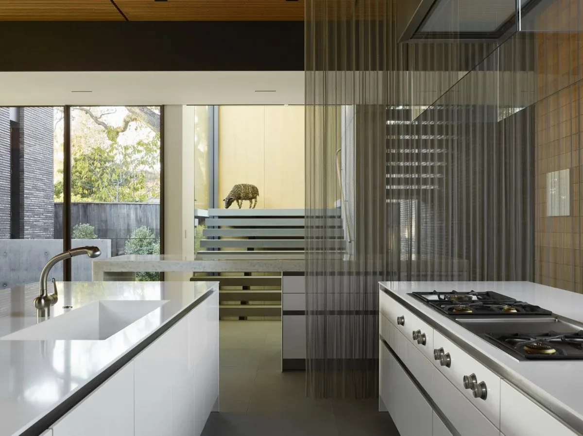 Kitchen interior with white cabinetry, integrated gas cooktop, and large windows overlooking an outdoor area.