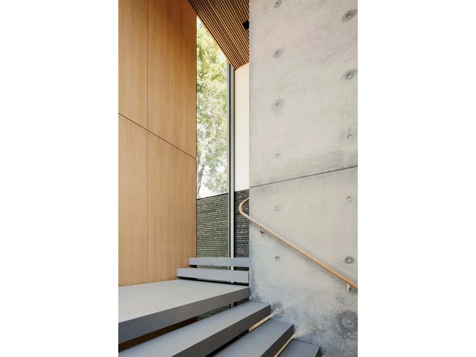 Interior view of a stairwell featuring exposed concrete walls, wood paneling, and a full-height window.