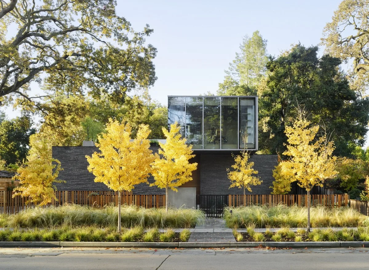 The Waverley house features a cantilevered glass upper volume over a brick lower volume with fall foliage landscaping at the front.