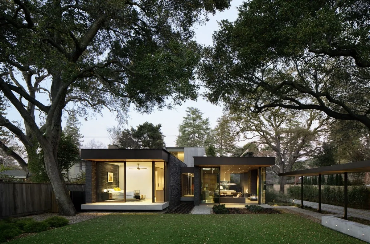 Modern residence with floor-to-ceiling glazing and flat roof, amid mature trees.