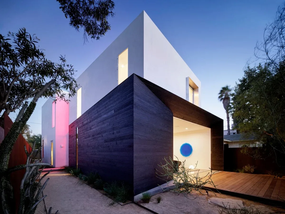 Two-story modern house with contrasting white upper and dark wood-clad lower sections photographed at dusk.