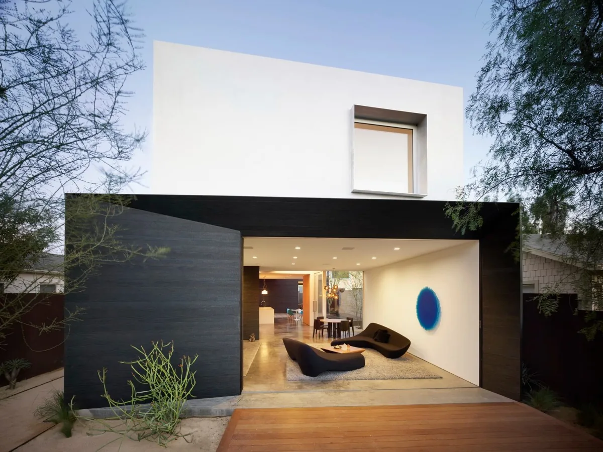 View of the home's exterior front showing a black-clad open living space with two modern black lounge chairs and a white upper level with a recessed window.