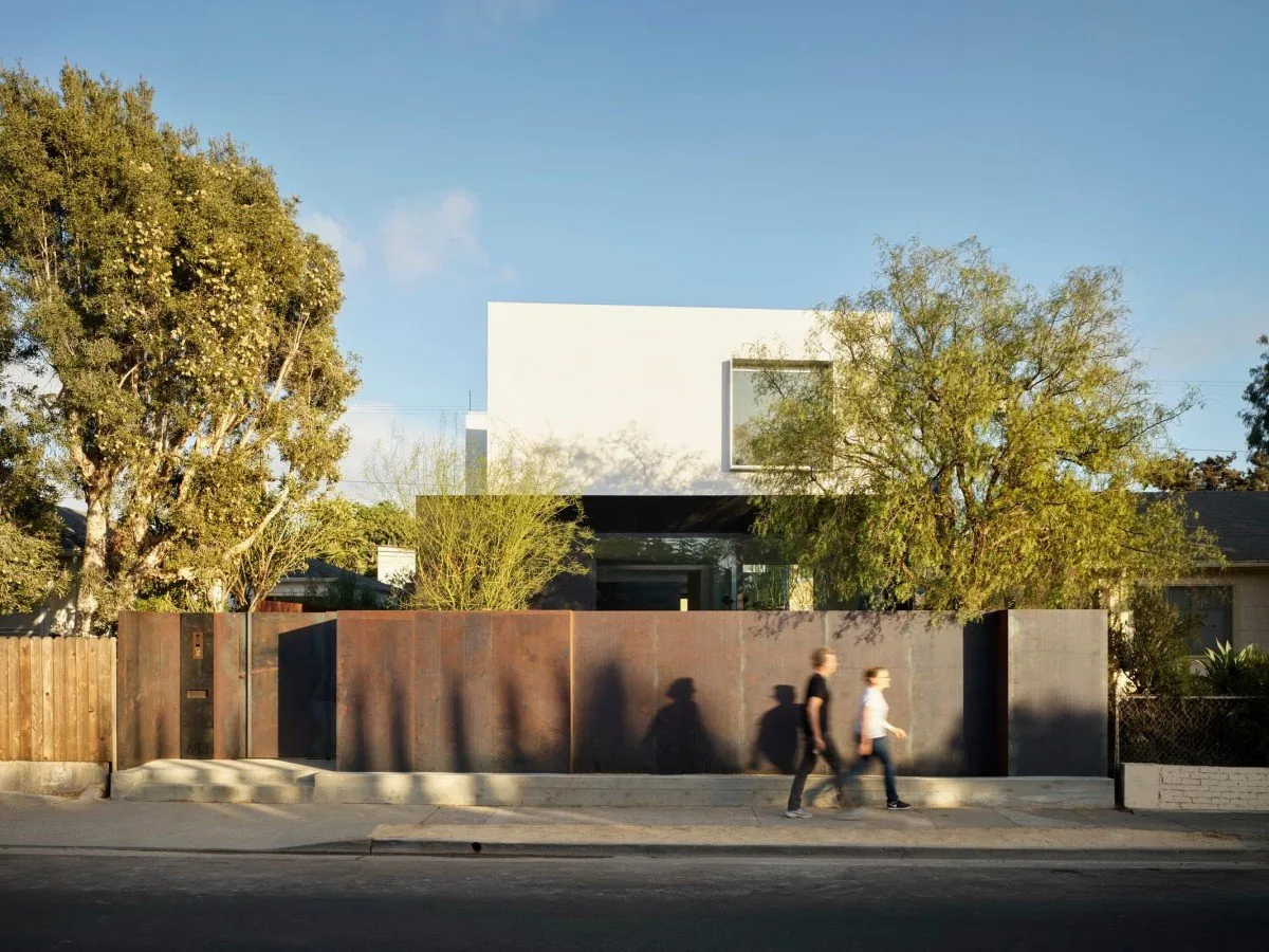 Modern house with a rust-colored metal fence and a white upper volume.