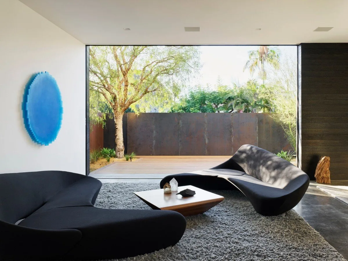 Living room with curved sofas and a large picture window opening to an outdoor deck and garden.
