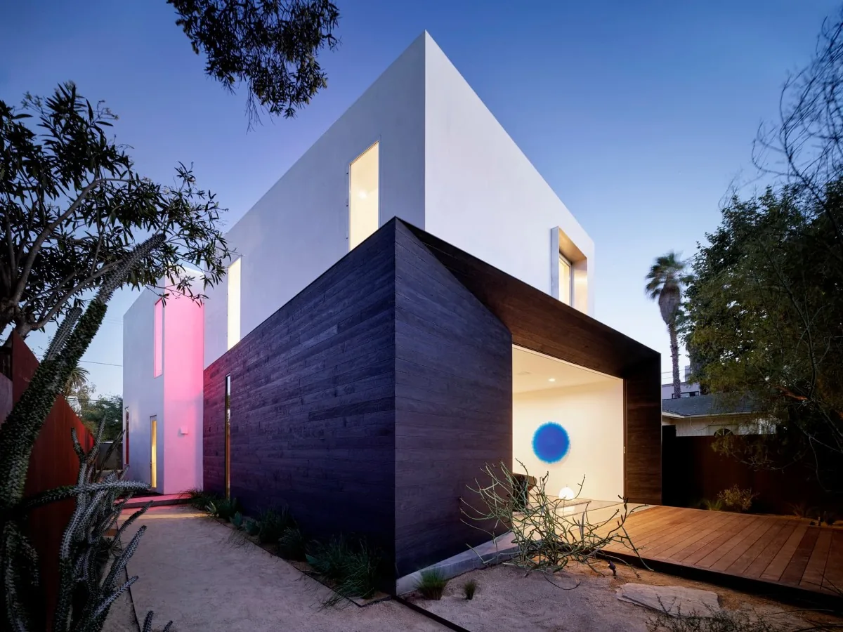 Exterior view of a modern two-story house with contrasting materials and a landscaped pathway at dusk.