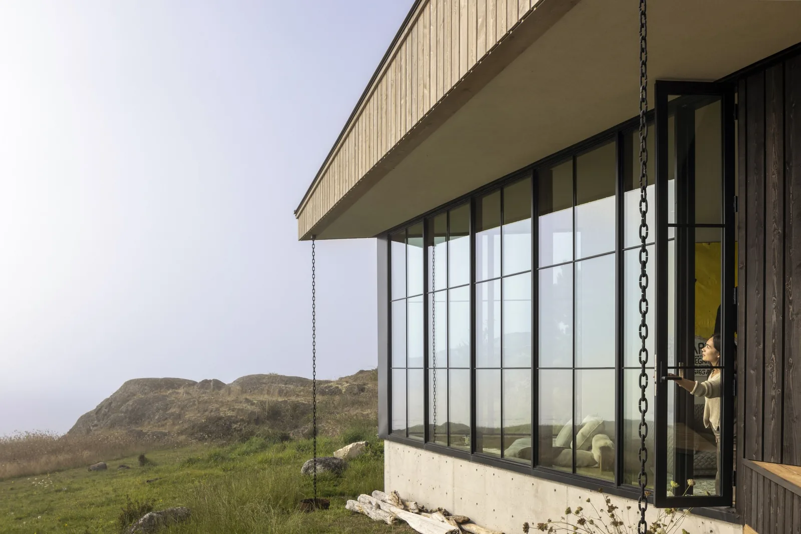 Modern house exterior with floor-to-ceiling glazing, black window frames, and vertical wood siding at False Bay project.