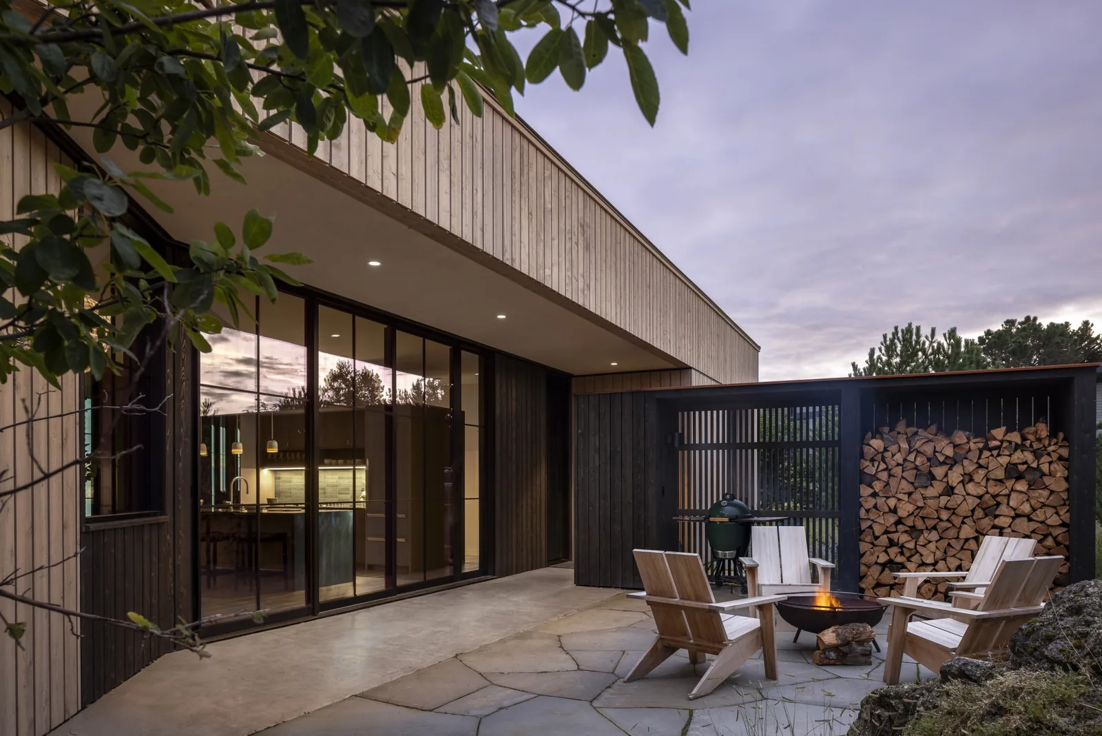 False Bay project features an outdoor fire pit area with stacked firewood and vertical wood siding on the home exterior.