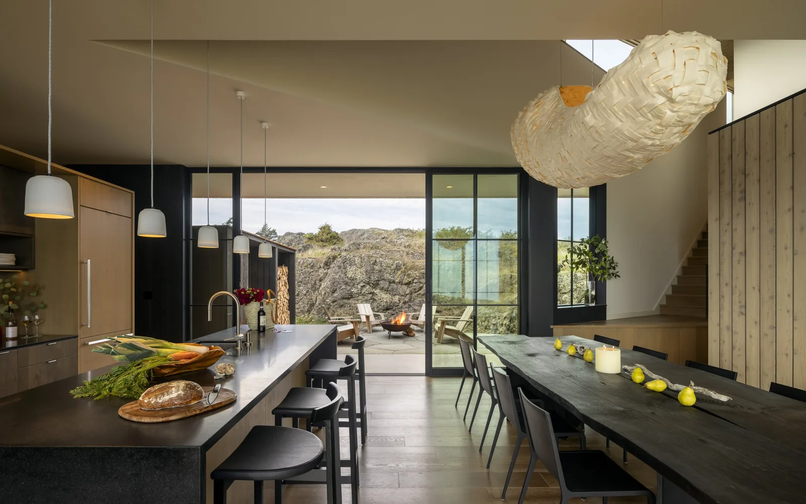 False Bay kitchen and dining area features wood paneling, black island, pendant lights, and floor-to-ceiling sliding glass doors to patio with fire pit.