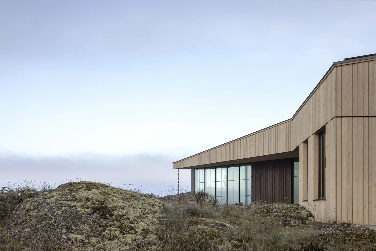 Modern house with vertical wood siding, large picture windows, and slanted roof on rocky terrain at False Bay.