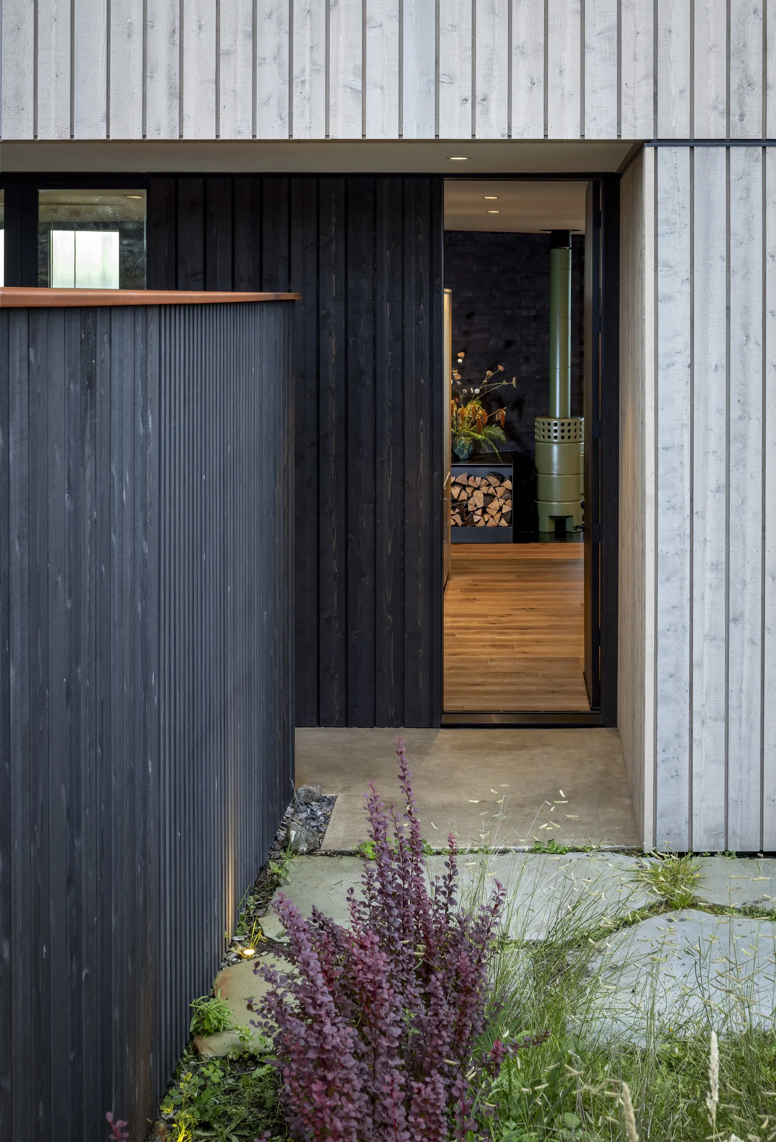 Entrance area with contrasting black and white vertical wood siding, showing an interior wood stove and wood floors.